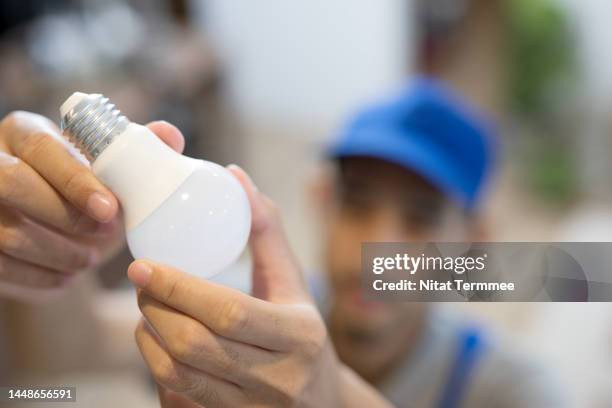 electrical repair and services on demand at your home. overhead view of male electrician reaching up to install or change a light bulb on the ceiling during on-site service at a customer's home. - luce led foto e immagini stock