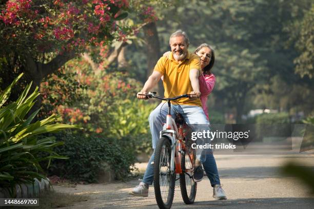 carefree excited senior couple riding bicycle in park - couple enjoyment stock pictures, royalty-free photos & images