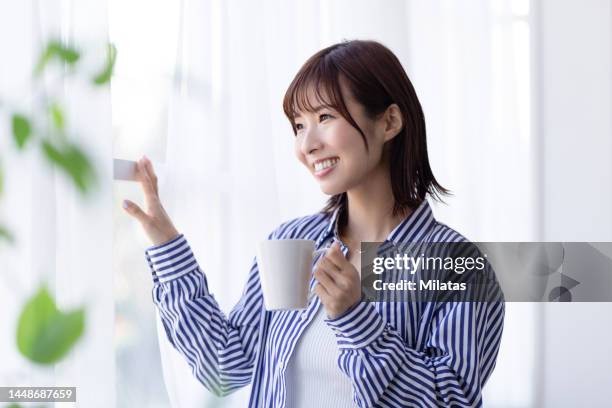 a woman standing by the window with a mug - 女性　日本人　笑顔　30代 ストックフォトと画像