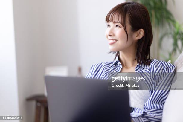 a woman sitting on the sofa and operating a computer - 女性　日本人　笑顔　30代 ストックフォトと画像