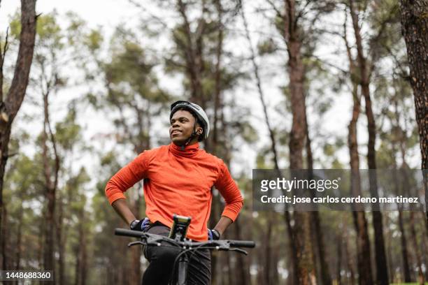 handsome african american man with a mountain bike standing in the forest, while looking around. - bicycle trail outdoor sports stock-fotos und bilder