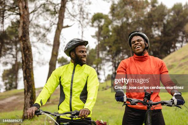 two friends laugh and enjoy a day with mountain bikes in nature while walking with the bike pushed by hand - friends cycling stock pictures, royalty-free photos & images