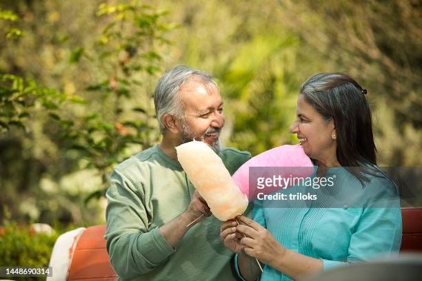 happy senior couple eating cotton candies in park - indulgence stock pictures, royalty-free photos & images