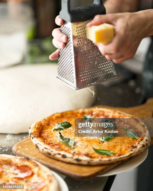 process of baking pizza. cook rubs parmesan cheese for pizza. pizza with cheese, sauce and basil. pizza on wooden board. working process in pizzeria. - grated stock pictures, royalty-free photos & images