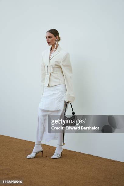 Guest wears large silver earrings with white feathers pendant, a white checkered cut-out chest / sleeveless / long tube dress from Jacquemus, a white...
