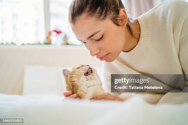 bound and trust between pet and owner. blond woman lying face to face with domestic cat with open mouth in white bed - meowing stock pictures, royalty-free photos & images