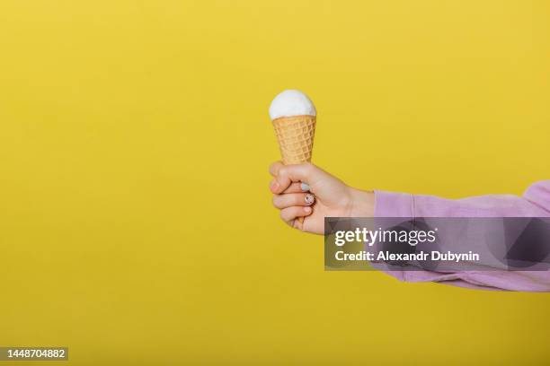 human hand holding ice cream cone on yellow background studio shot with copy space. - food advertisement stock pictures, royalty-free photos & images