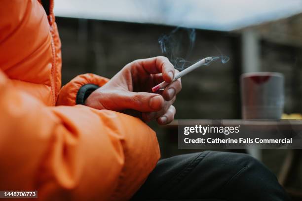 close-up of a mans hand holding a slim straight cigarette - rook stockfoto's en -beelden