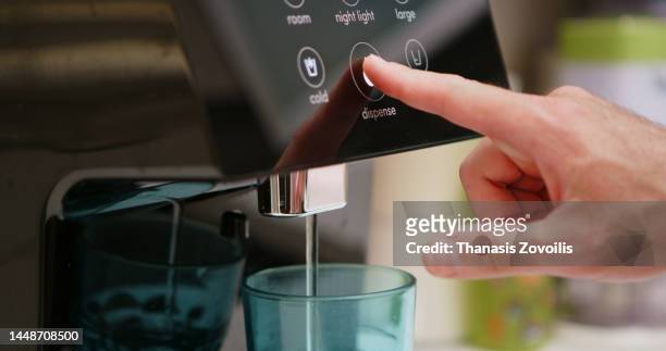 side view of man's hand pressing a touch button screen of a house water dispenser and purring water in glass. - 浄水 ストックフォトと画像