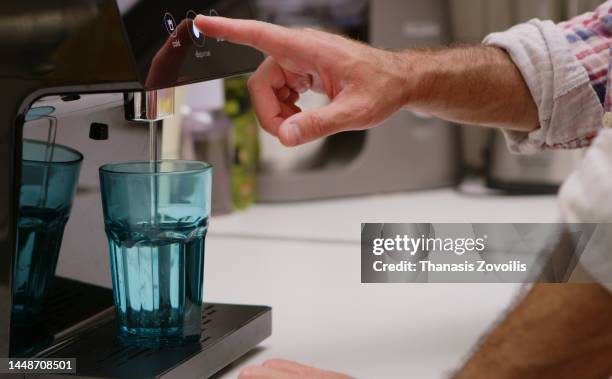 side view of man's hand pressing a touch button screen of a house water dispenser and purring water in glass. - purified water 個照片及圖片檔