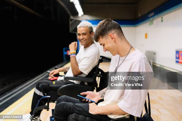 portrait of latin american students men on wheelchair smiling on subway platform with backpacks. - fauteuil handicap stock pictures, royalty-free photos & images
