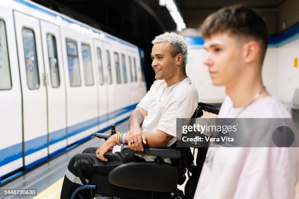 portrait of latin american students men on wheelchair waiting on subway platform with backpacks. - fauteuil handicap stock pictures, royalty-free photos & images