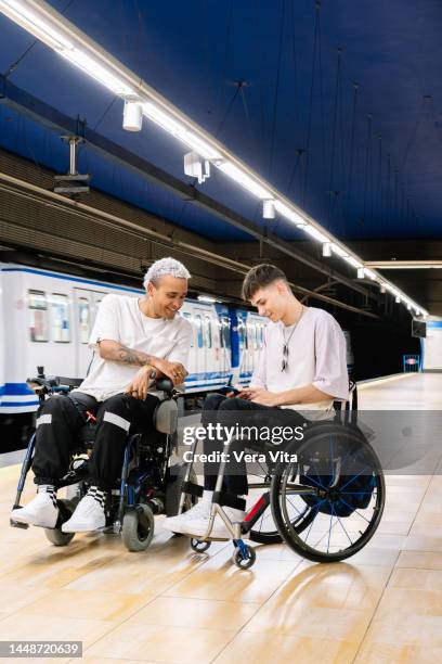 latin american students men on wheelchair waiting on subway platform using phone. - fauteuil handicap stock pictures, royalty-free photos & images