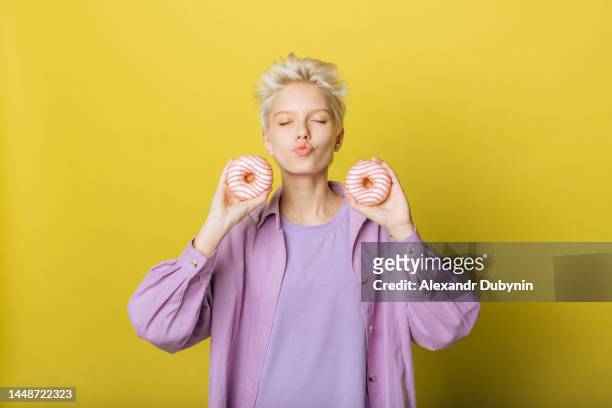 young young girl holding donuts in her hands on a yellow background - portrait cuisine stock-fotos und bilder