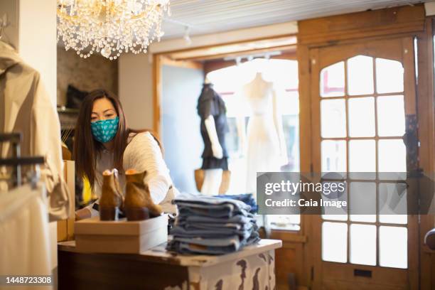 female shop owner in face mask arranging display in clothing boutique - pile ou face stock-fotos und bilder