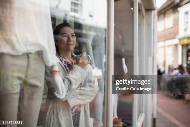 female shop owner with tea looking out shop window - セブンオークス ストックフォトと画像