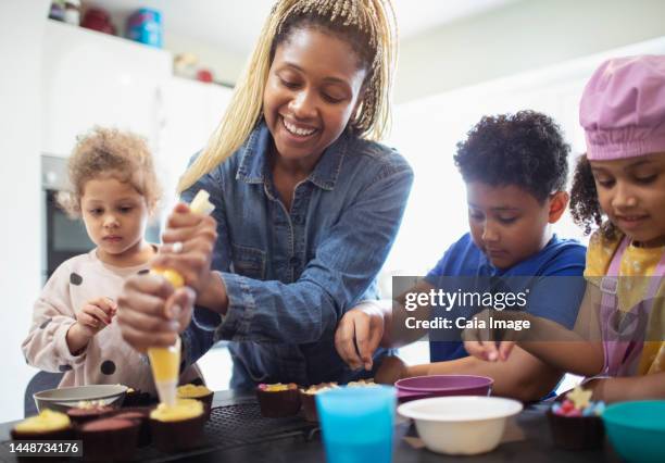 happy mother and kids decorating cupcakes in kitchen - bruder schwester kochen stock-fotos und bilder