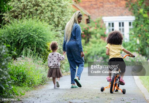 mother and daughters walking and riding bicycle in driveway - london bikes stock pictures, royalty-free photos & images