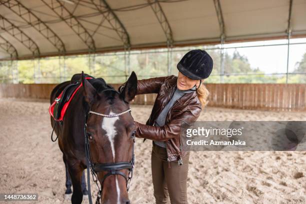 jinete caucásico adulto maduro cuidando de su caballo marrón en una pista de equitación - riding hat fotografías e imágenes de stock