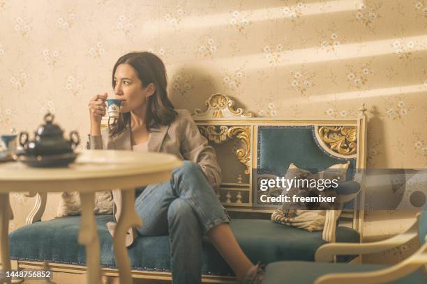 donna bere il caffè a casa  - antique sofa styles foto e immagini stock