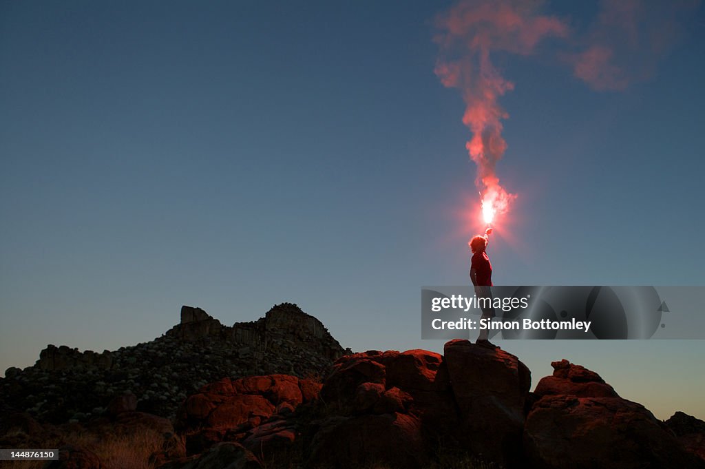 Man holding flare at sunset.
