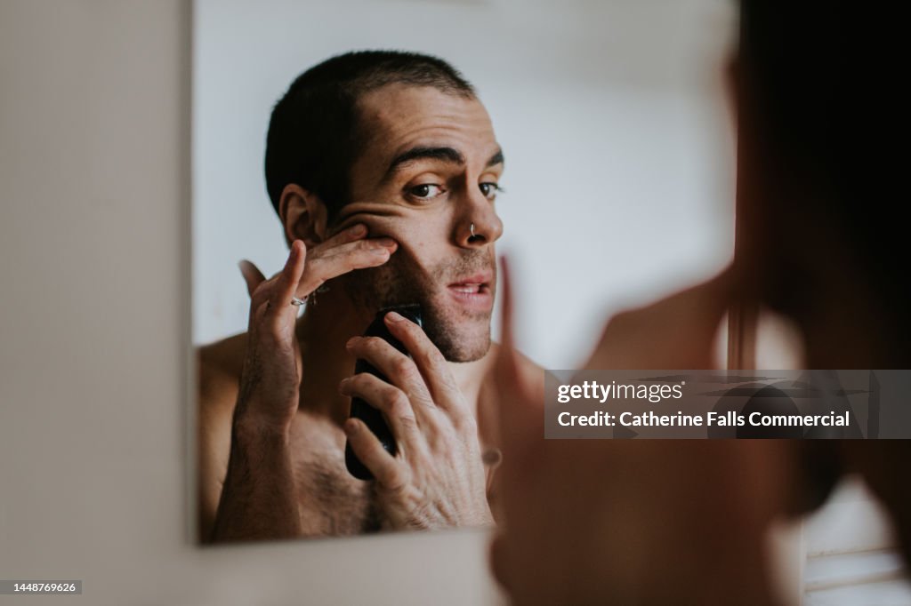 A man shaves his face with an electric shaver