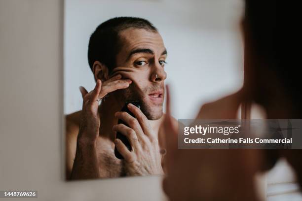 a man shaves his face with an electric shaver - bathroom mirror 個照片及圖片檔
