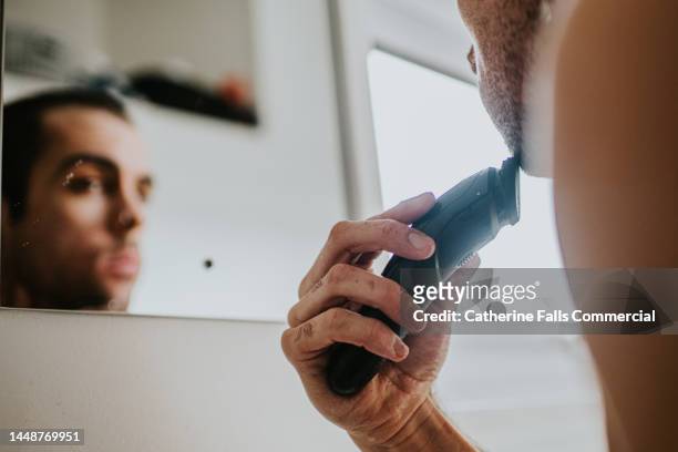 a man shaves his face with an electric shaver - beard trimmer stock pictures, royalty-free photos & images