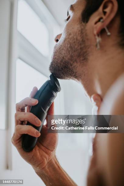 a man shaves his face with an electric shaver - man shaving foam stock pictures, royalty-free photos & images