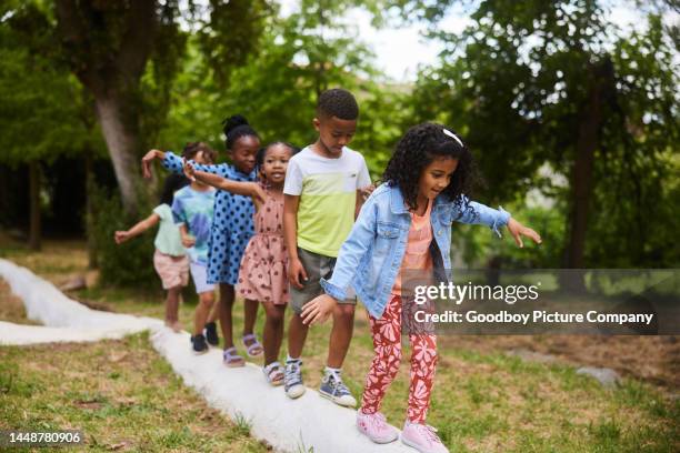 little children balancing on a ledge while playing in a park - kids in a row stock pictures, royalty-free photos & images