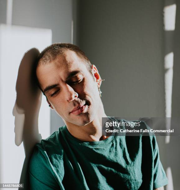a man looks serene and content as he rests his head on a wall, casting a shadow. - relief emotion fotografías e imágenes de stock