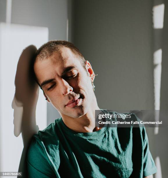 a man looks serene and content as he rests his head on a wall, casting a shadow. - relief emotion stock pictures, royalty-free photos & images