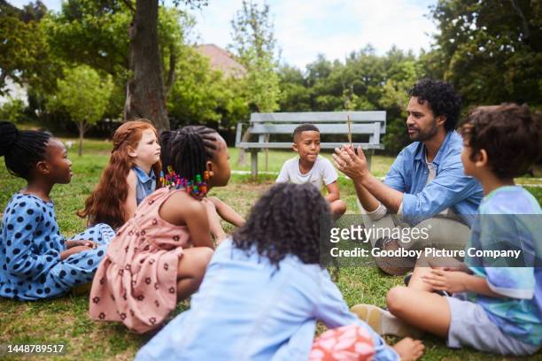 insegnante che parla con i giovani studenti fuori su un po 'di erba - bambini seduti in cerchio foto e immagini stock