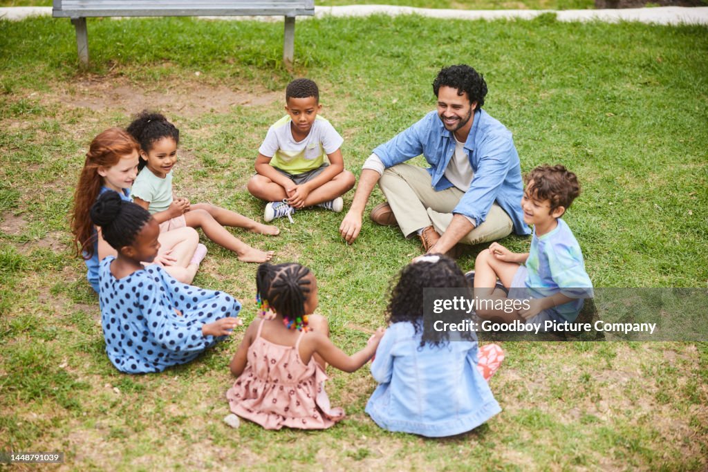 Smiling teacher talking with young students outside on a some grass