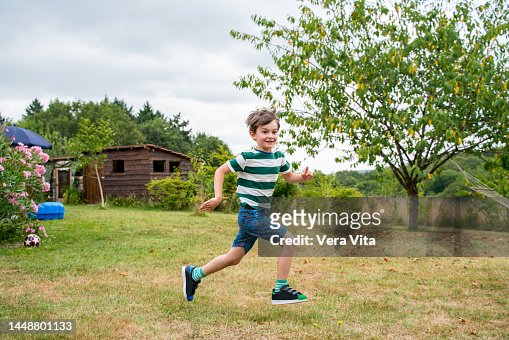 Little boy in green casual clothes running on the garden in holidays.