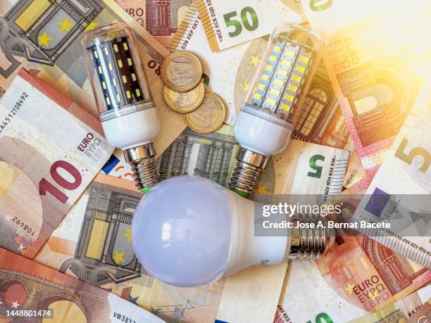 low consumption electric light bulbs and euro banknotes and coins. - crisis de petróleo fotografías e imágenes de stock
