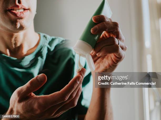 a man applies lotion to his hand - mann creme stock-fotos und bilder