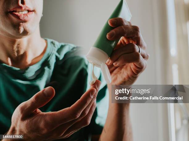 a man applies lotion to his hand - creme tube imagens e fotografias de stock