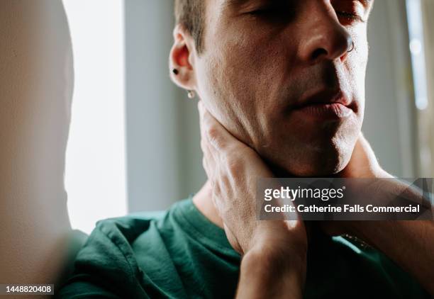 a man cups his neck and throat with his hands - streptococcus stock-fotos und bilder