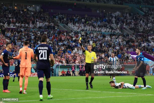 Referee Daniele Orsato shows a yellow card to Dominik Livakovic of Croatia after his collision with Julian Alvarez of Argentina leading to a penalty...