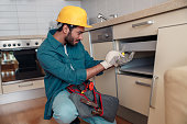 Focused professional worker in uniform is assembling furniture on kitchen. Repair concept