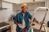 Smiling handyman is standing on ladder in kitchen and holding a screwdriver