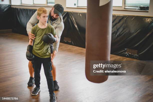 male trainer is engaged in boxing with a teenager in the gym(punching bag) - arts martiaux stock pictures, royalty-free photos & images