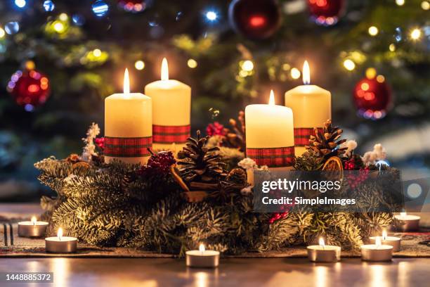 advent wreath with four burning candles on the table in front of the christmas tree. - christmas candles stock-fotos und bilder