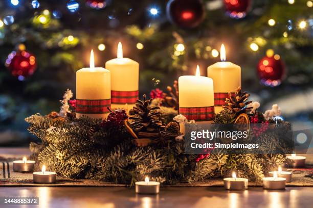 advent wreath with four burning candles on the table in front of the christmas tree. - corona di fiori composizione foto e immagini stock