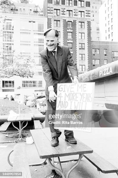View of a demonstrator, in a suit and mask holds a sign while standing on a picnic table during a protest against Operation Rescue , organized by...