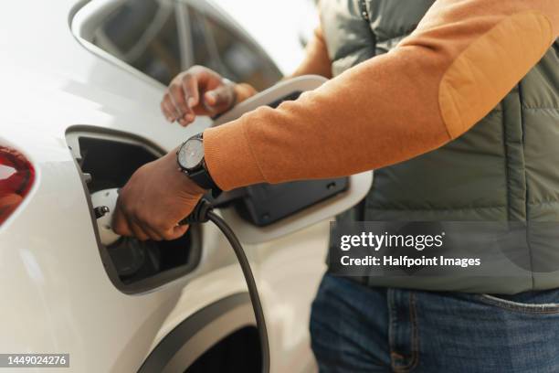 close-up of young multiracial man charging electric car. - elektrische auto stockfoto's en -beelden