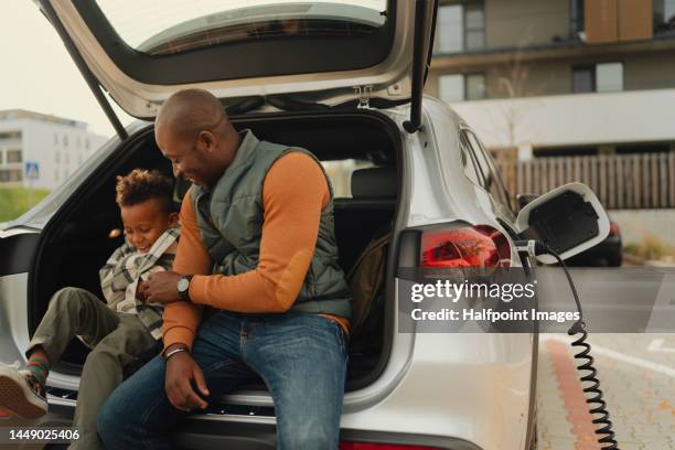 father with his son waiting while their electric car charging. - auto familie stock-fotos und bilder