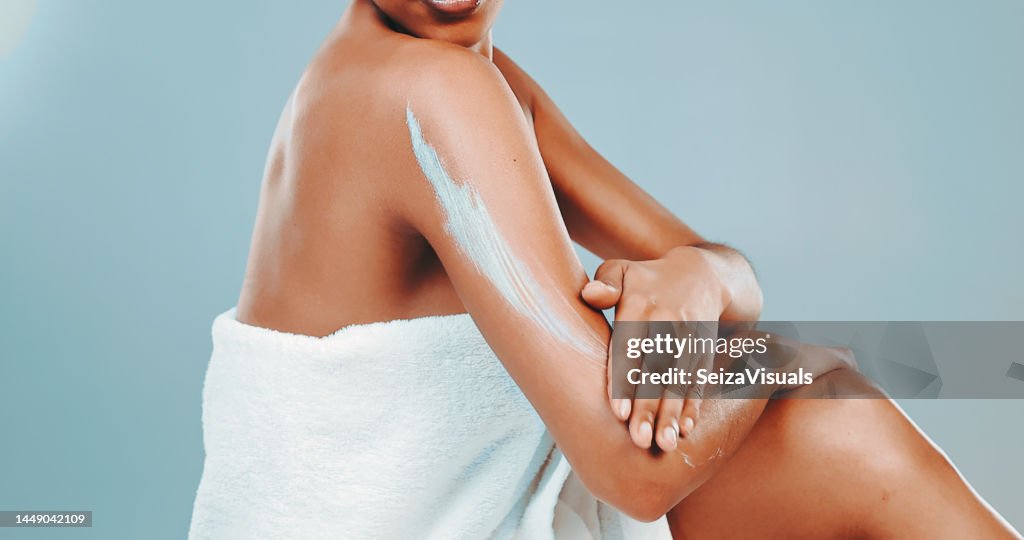 Foto de estudio de una mujer envuelta en una toalla aplicando loción corporal