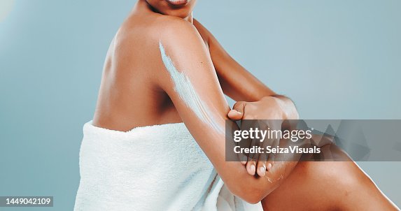 Foto de estudio de una mujer envuelta en una toalla aplicando loción corporal Foto de estudio de una mujer envuelta en una toalla aplicando loción corporal